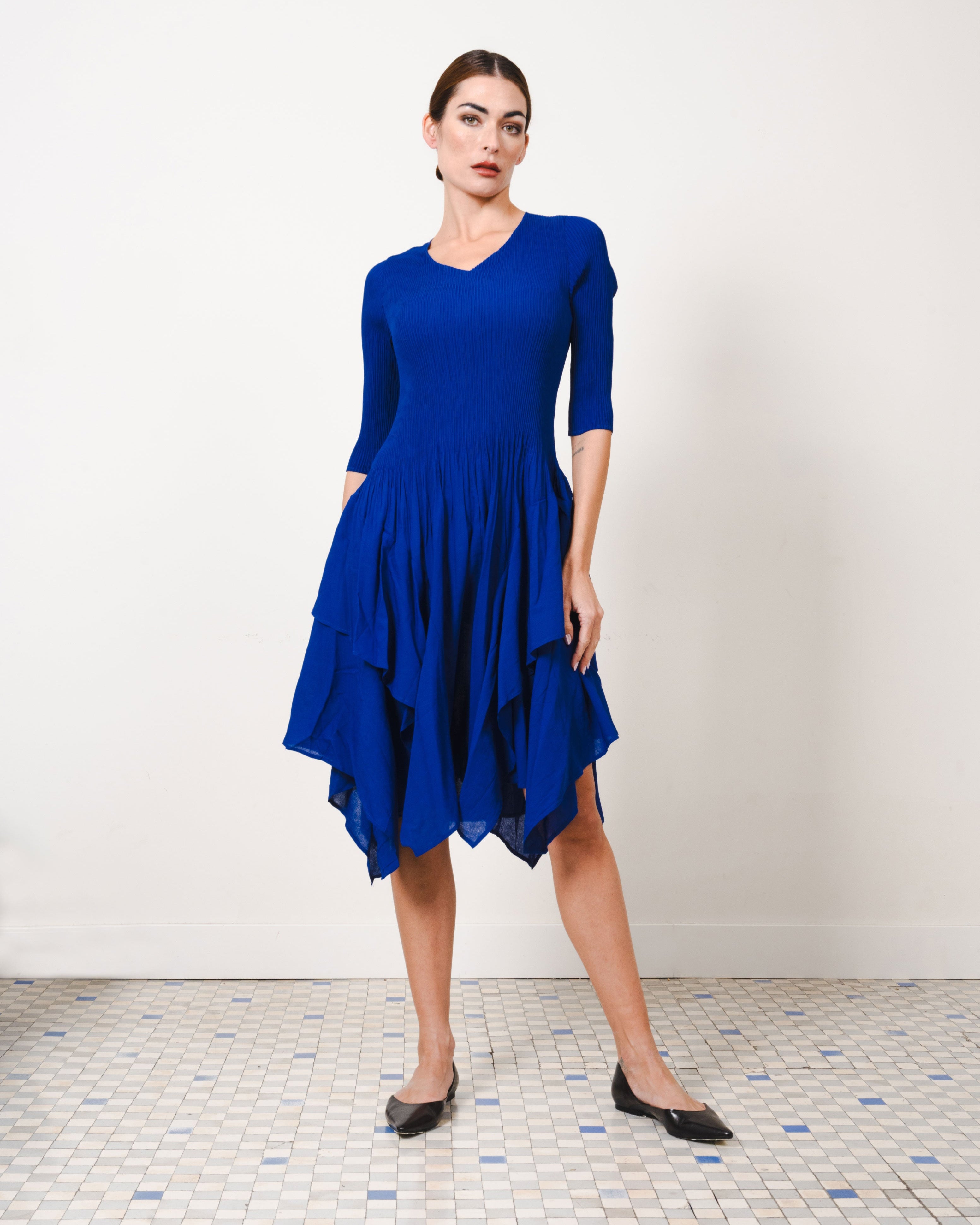 Woman wearing a blue dress standing on a tiled floor with a white wall background